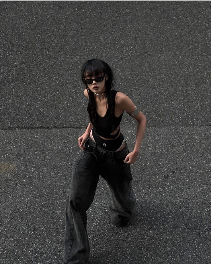 Woman with black hair and sunglasses wearing a crop top and baggy jeans outdoors