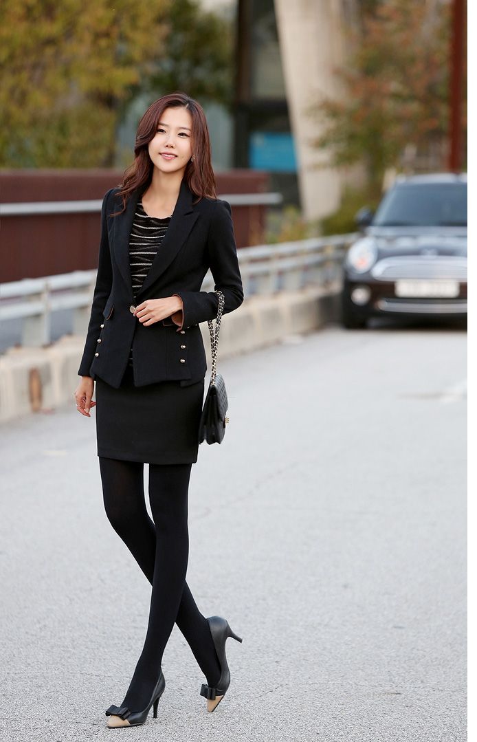 Woman in a black suit and skirt with tights and high heels outdoors