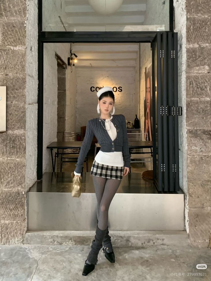 Woman in a plaid skirt, cropped cardigan, and leg warmers standing indoors