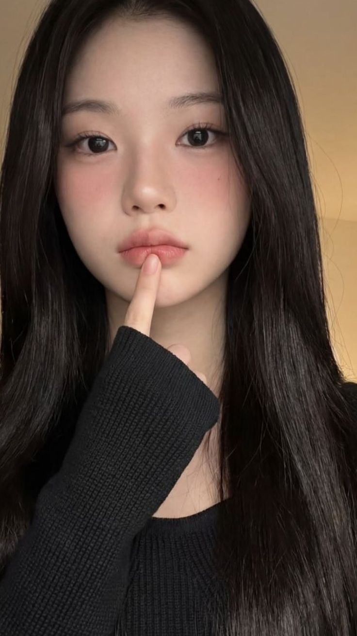 Woman with long black hair and pink blush wearing a black sweater