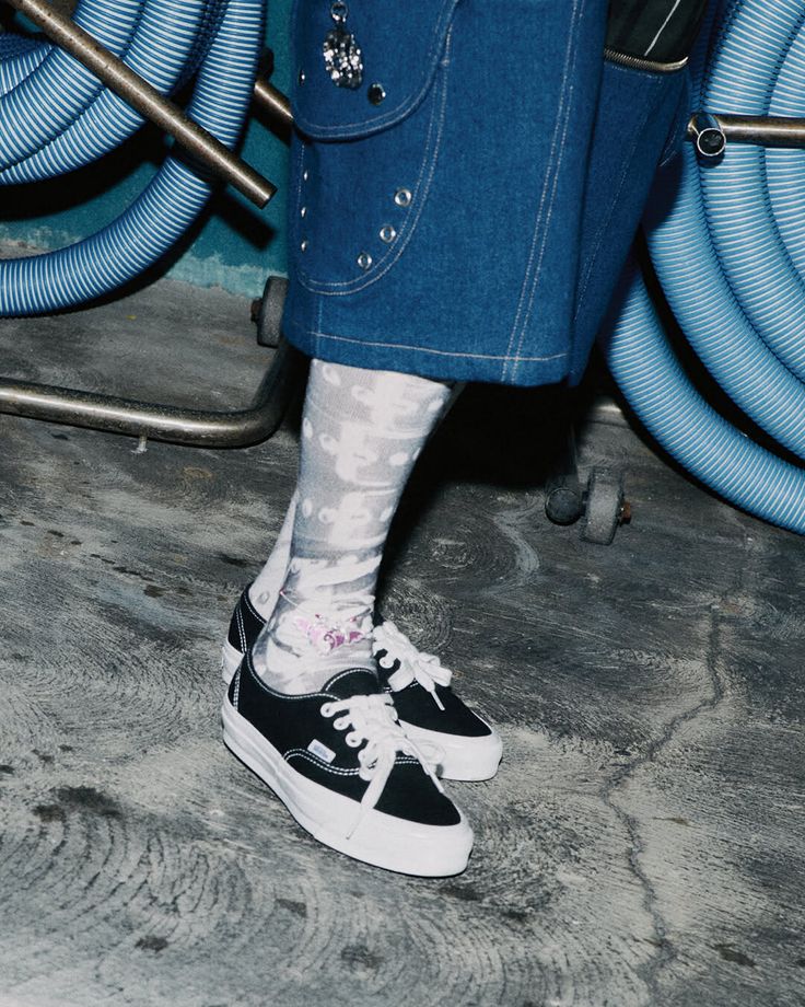 Person wearing denim shorts, patterned socks, and black sneakers on a concrete floor