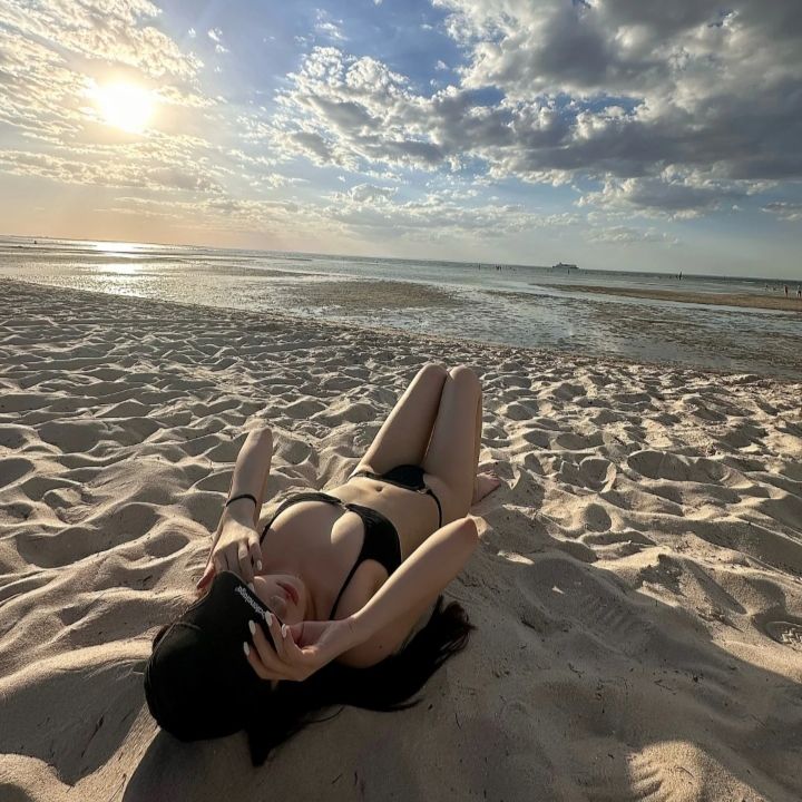 Woman in a black bikini lying on a sandy beach at sunset
