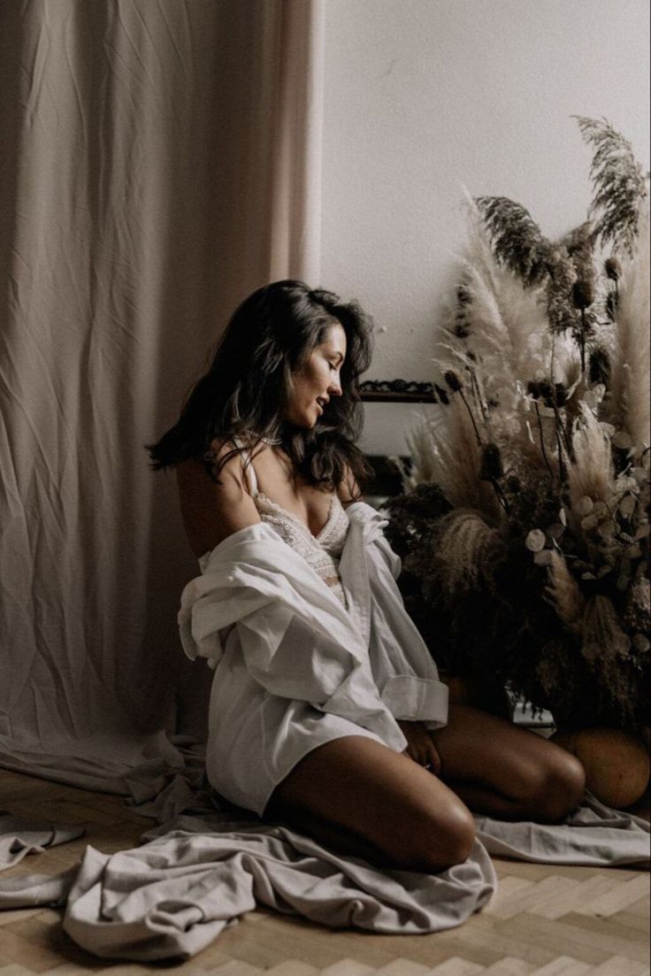Woman in a white shirt and lace bra kneeling on the floor with dried plants
