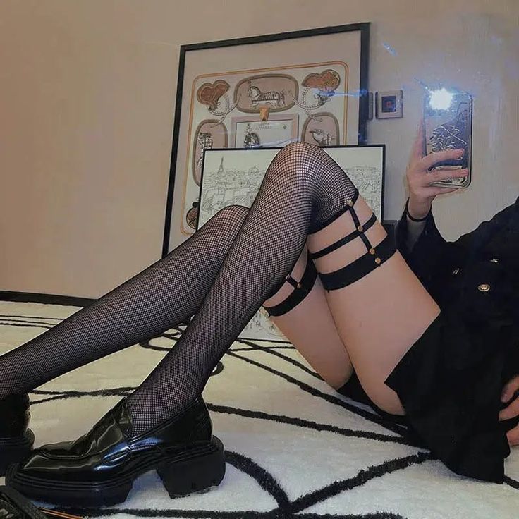 Person in fishnet stockings and black shoes taking a mirror selfie