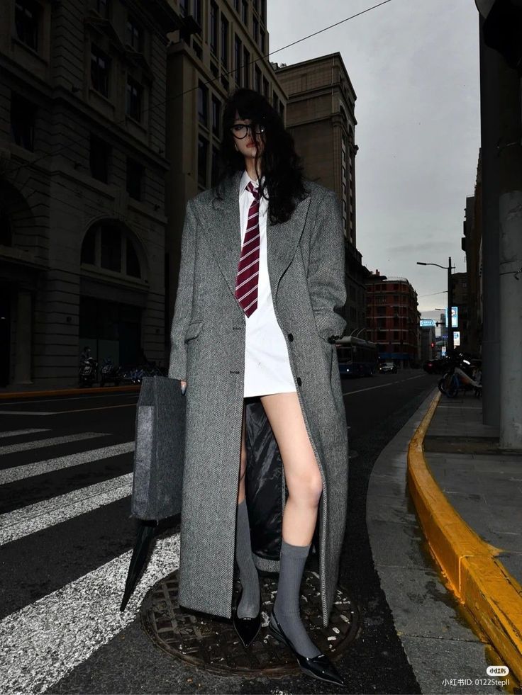 Person in a long coat, white shirt, and tie on a city street