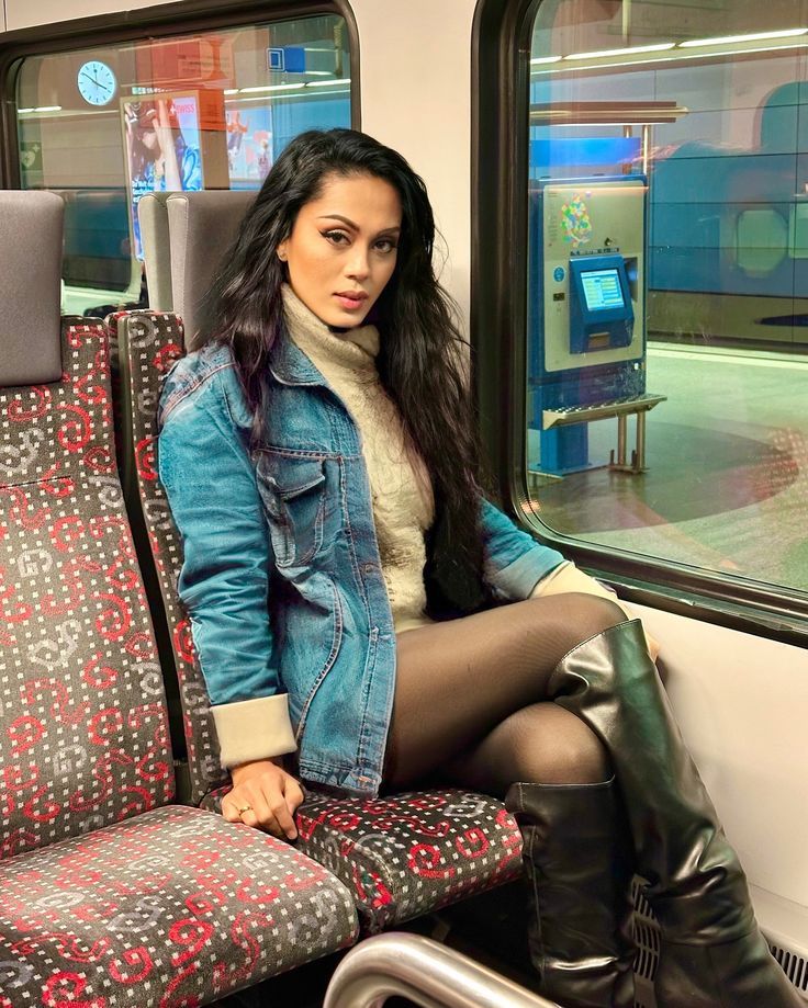 Woman with long black hair wearing a denim jacket and black tights inside a train