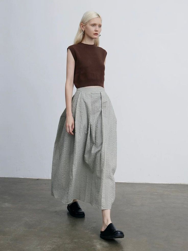 Woman with blonde hair wearing a brown top and long skirt indoors