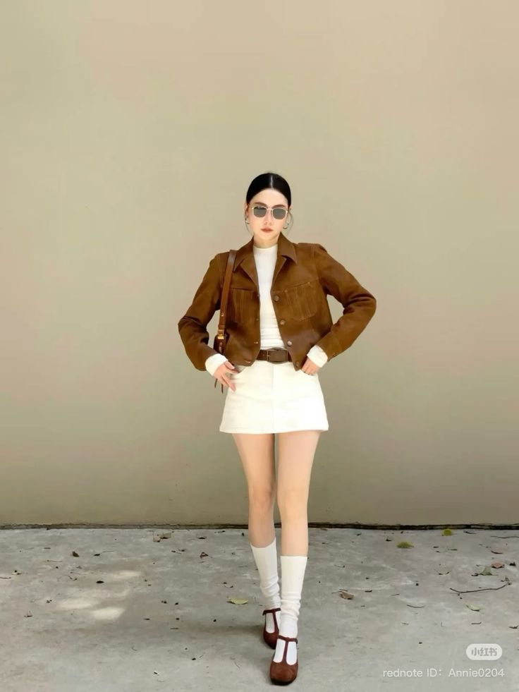Woman in a brown jacket and white skirt posing outdoors