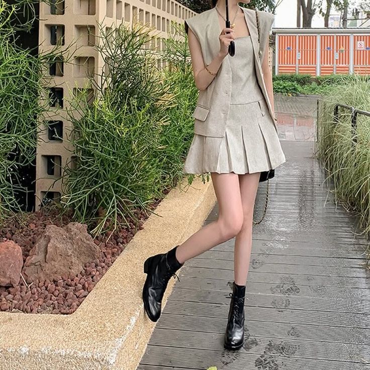 Woman in a pleated skirt and sleeveless vest with black boots outdoors