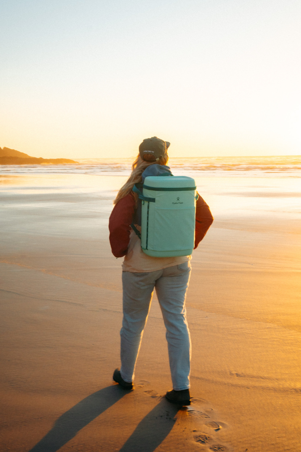 Person with a backpack on a beach at golden hour, viewed from behind
