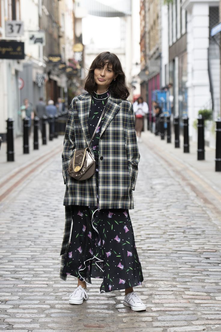 Woman in a plaid blazer and floral dress on a cobblestone street