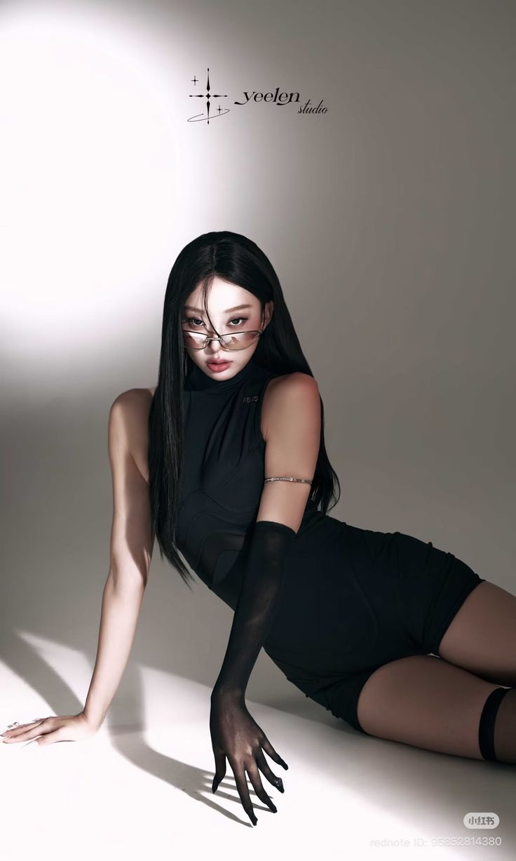 Woman with long black hair and sunglasses in a black outfit posing in a studio