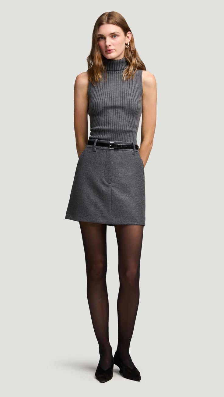 Woman in a gray ribbed turtleneck top and mini skirt with black tights
