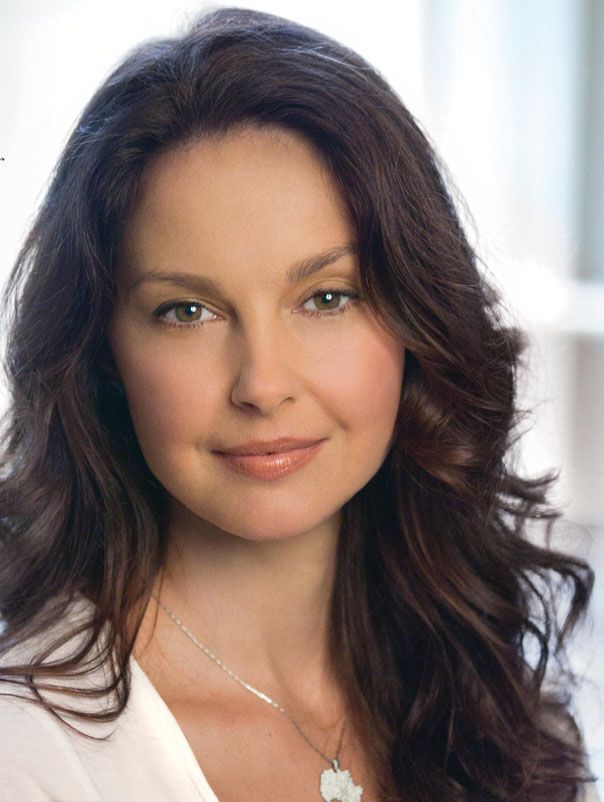 Woman with long brown hair and green eyes wearing a white shirt and silver necklace