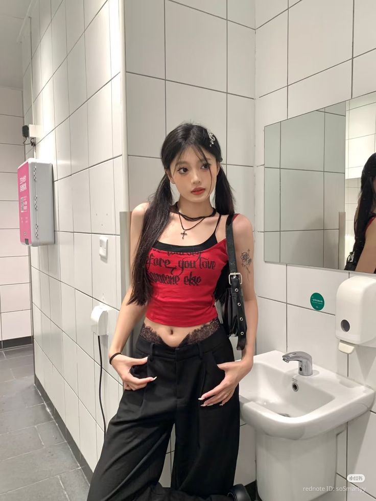 Woman with pigtails in a red crop top and black pants in a bathroom