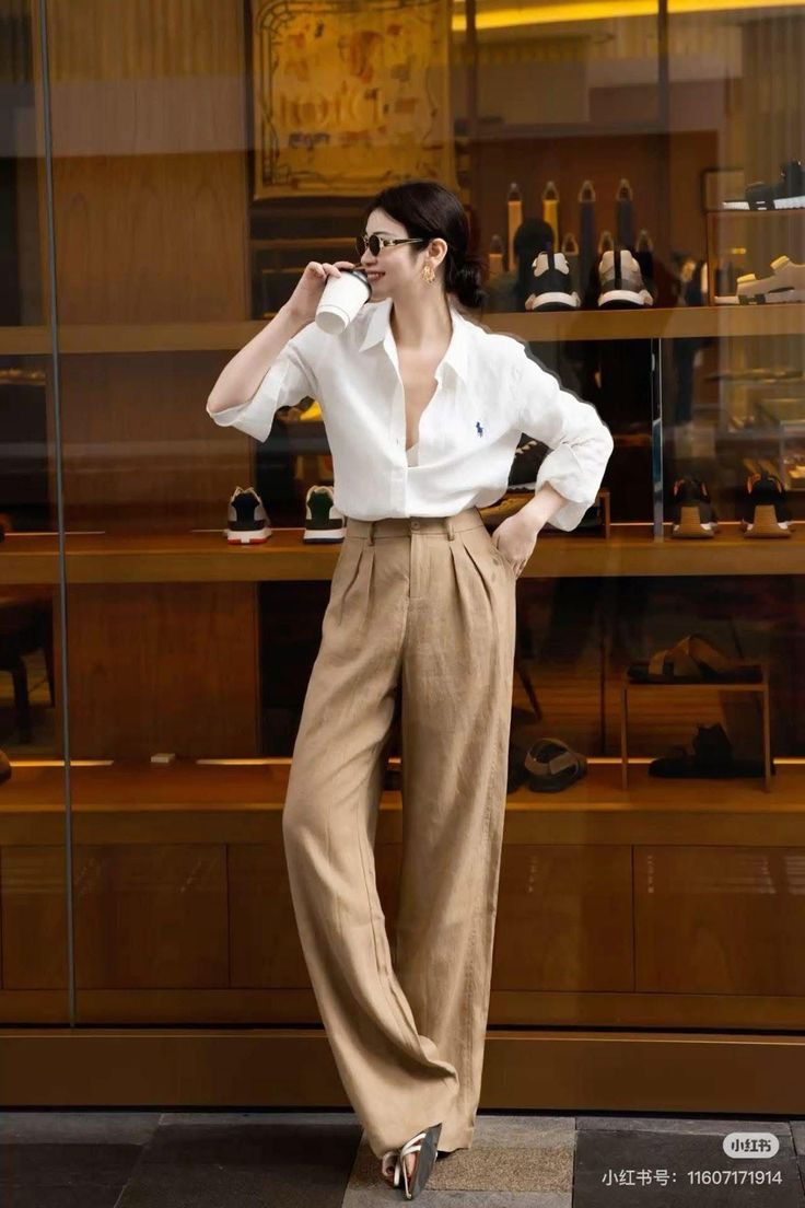 Woman in a white shirt and wide leg pants holding a cup indoors