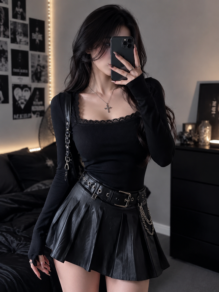 Woman in a black top and pleated skirt taking a mirror selfie in a dark room