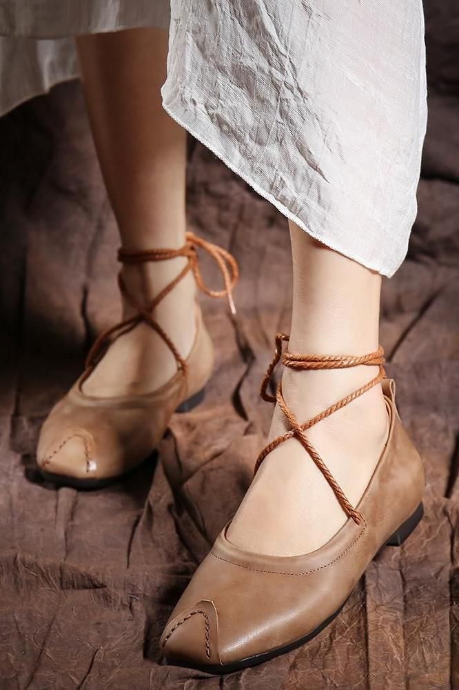 Person wearing brown lace-up flats and a white dress on a brown background