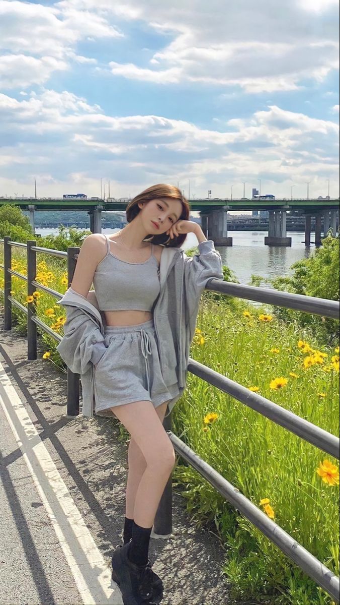 Woman in a grey crop top and shorts leaning on a railing by a river