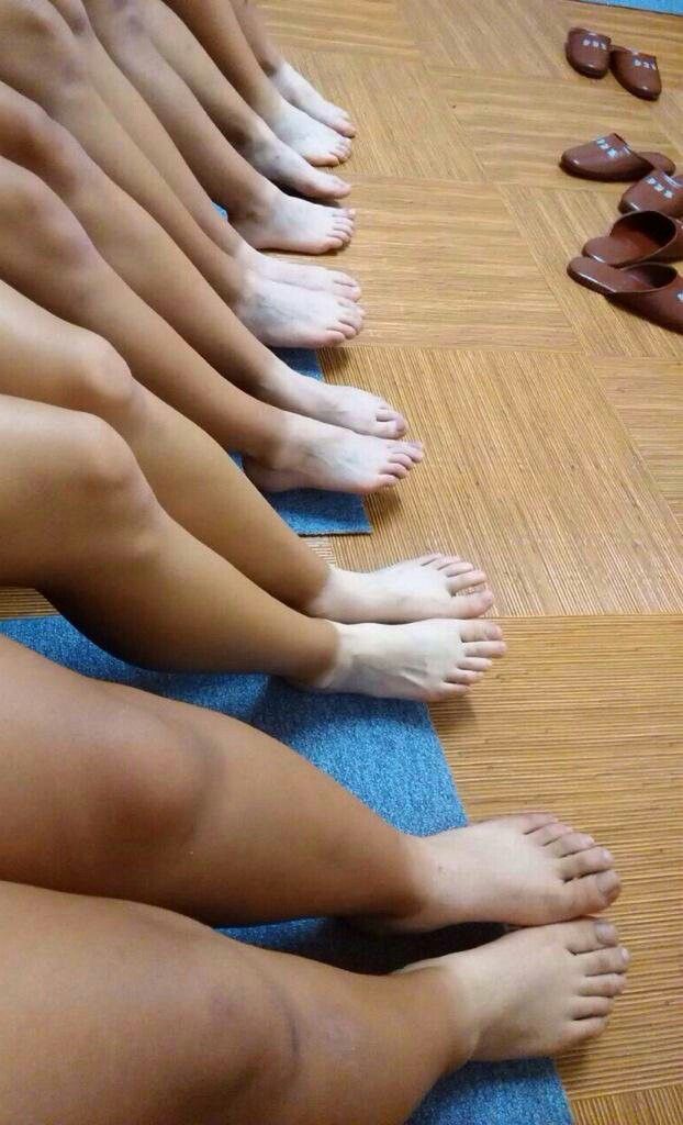 Multiple people's legs and feet with tan lines on a blue mat and wooden floor