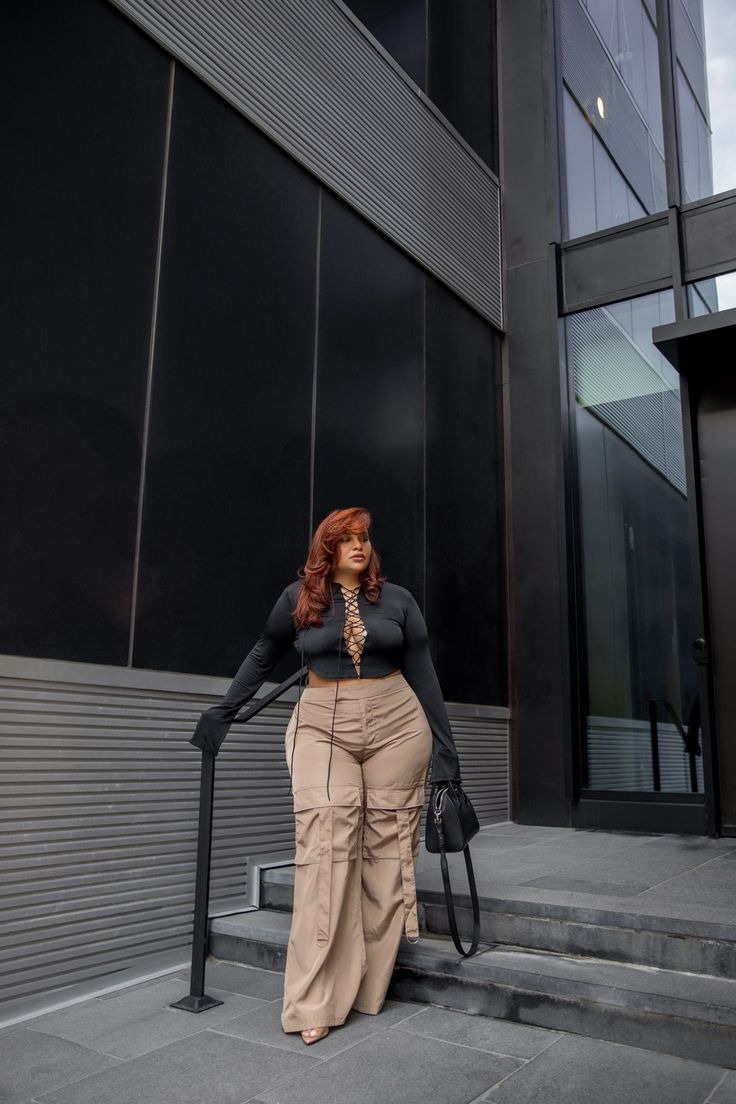 Woman with long red hair wearing a black crop top and cargo pants outdoors