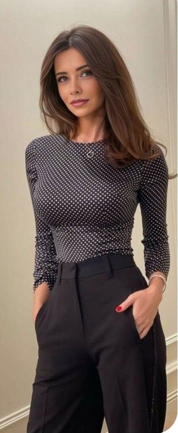 Woman with long brown hair wearing a polka dot top and black pants indoors