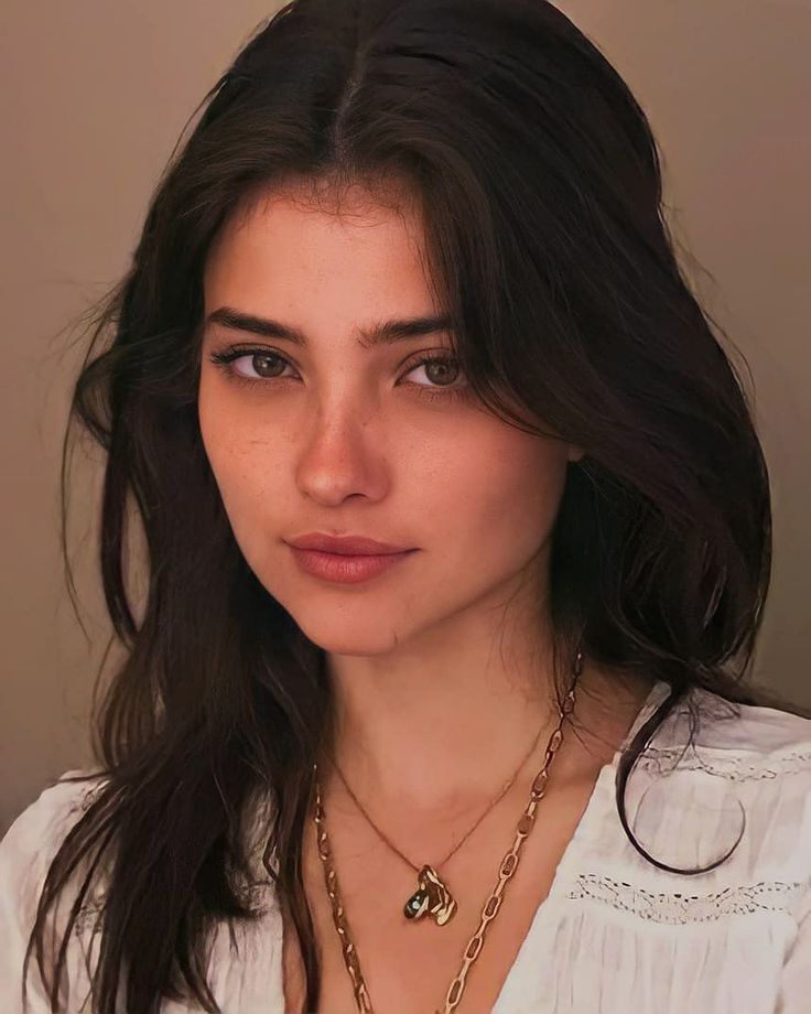 Woman with long dark hair and freckles wearing a white shirt and gold necklace