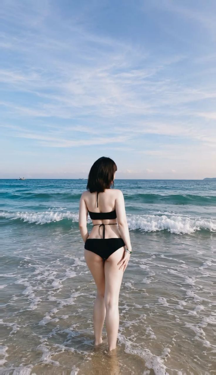 Woman in a black bikini standing in the ocean with her back to the camera