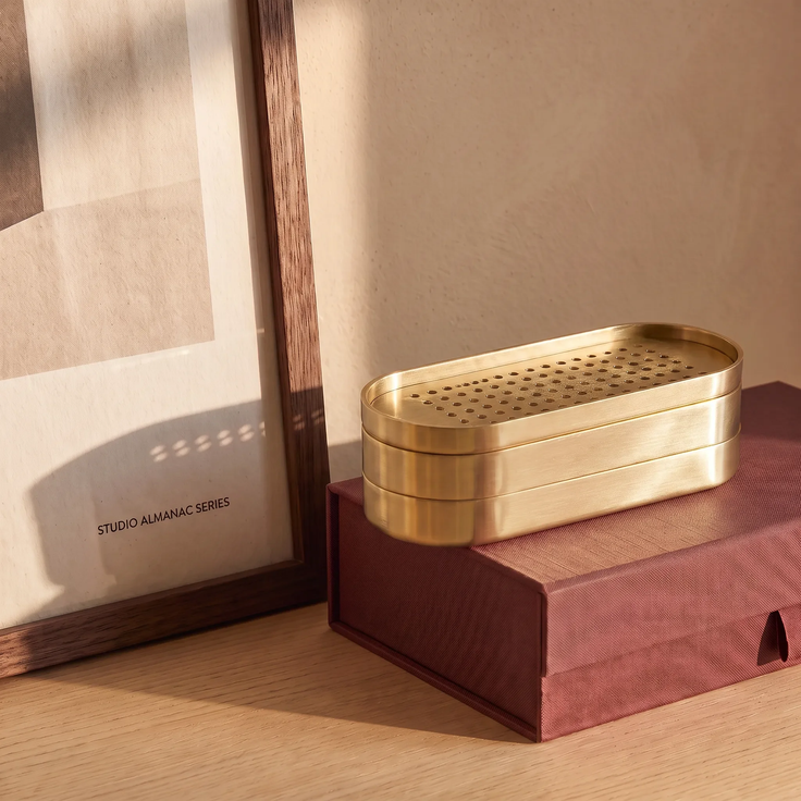 Brass container with a perforated lid on a red box next to a framed picture