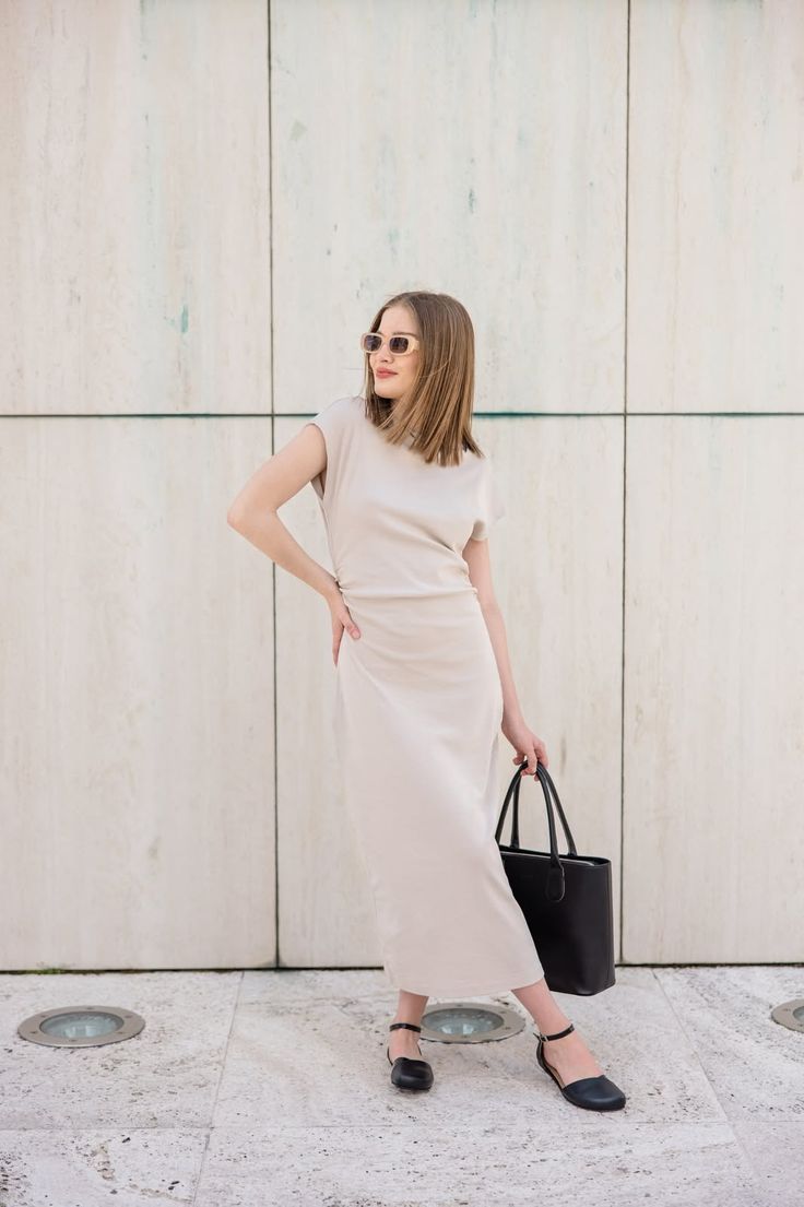 Woman in a beige midi dress and sunglasses holding a black handbag outdoors
