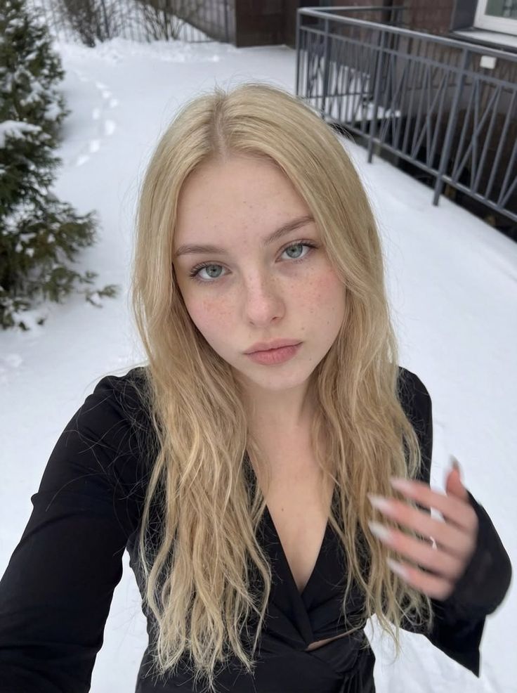 Blonde woman with freckles in a black dress outdoors in the snow