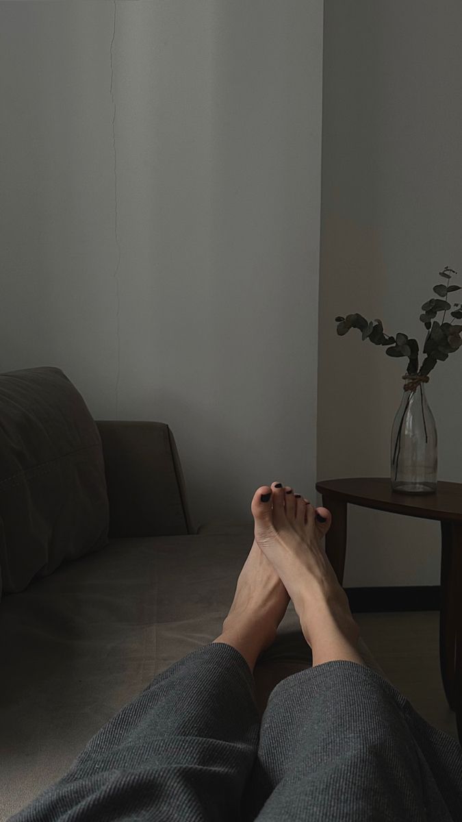 Person's feet with black nail polish resting on a couch in a dimly lit room