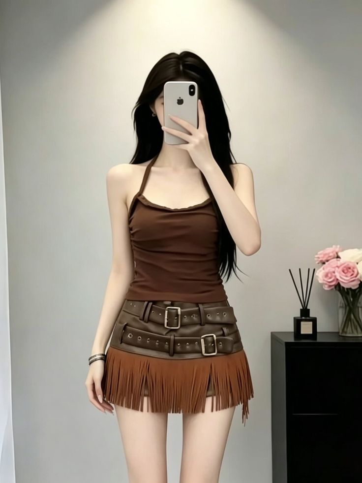 Person with long black hair taking a mirror selfie in a halter top and fringe skirt