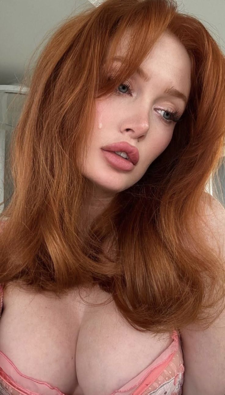 Woman with red hair and a teardrop on her cheek, wearing pink lingerie