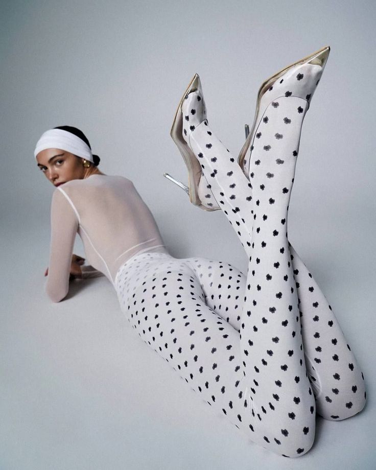 Woman in polka dot leggings and sheer top lying on a white surface