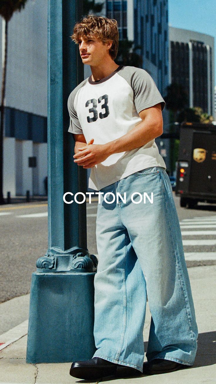 Man in a raglan t-shirt and baggy jeans standing on a city street