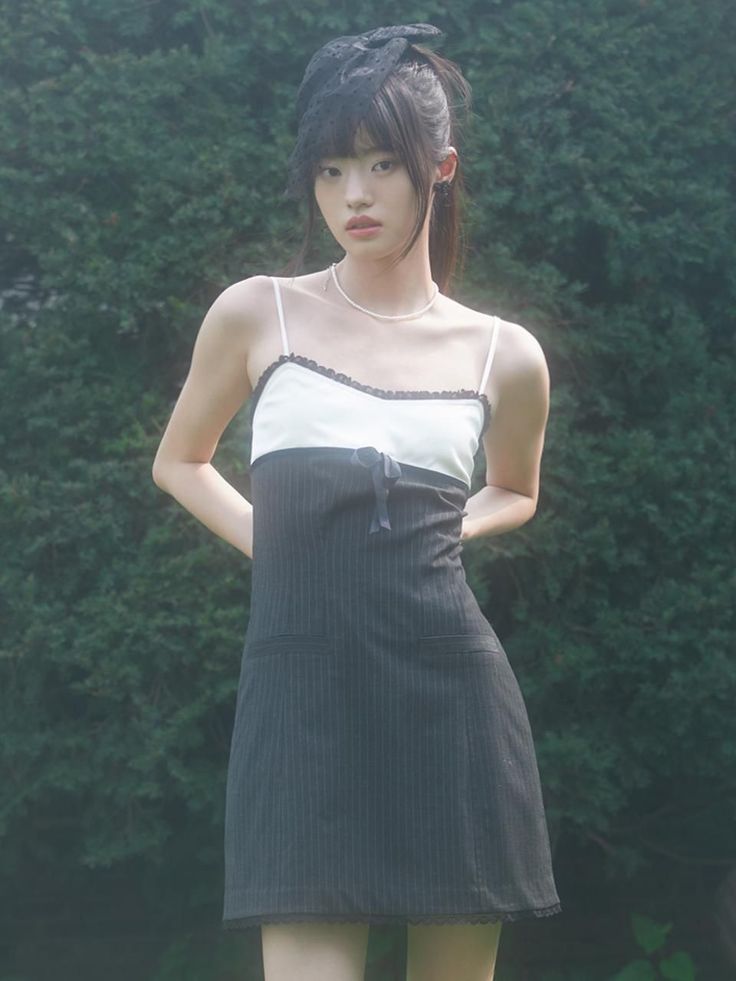 Woman in a black pinstripe dress and hat with a pearl necklace outdoors