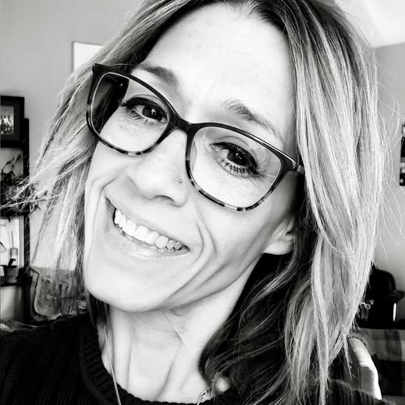 Woman with glasses and short hair smiling in a black and white portrait