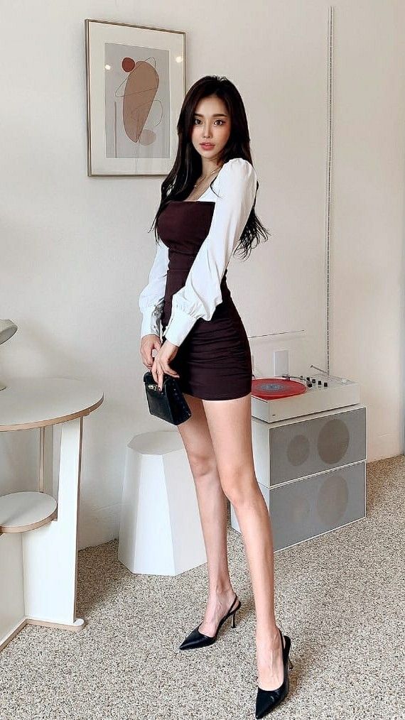 Woman in a brown mini dress and white long-sleeve top holding a black handbag
