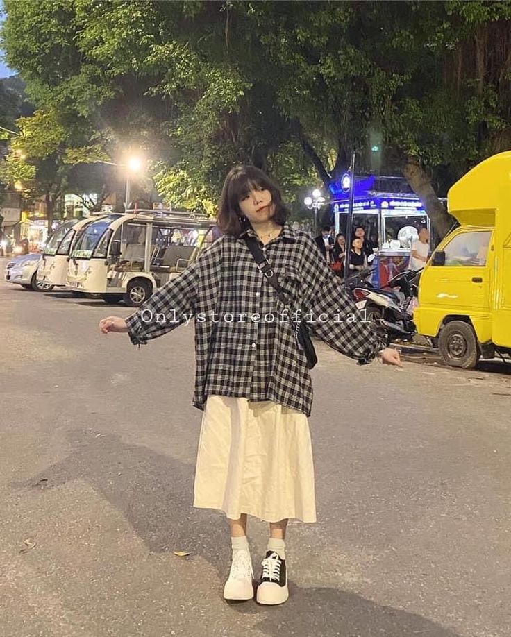 Woman in a plaid shirt and midi skirt standing on a street at night
