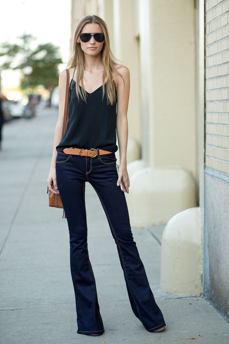 Woman in a black camisole and flared jeans with sunglasses on a street