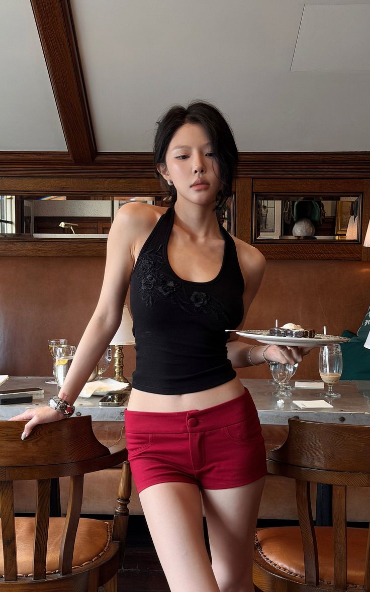 Woman in a black halter top and red shorts holding a tray of desserts