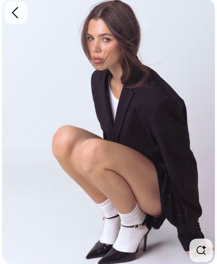 Woman in a black blazer and white socks squatting in a studio