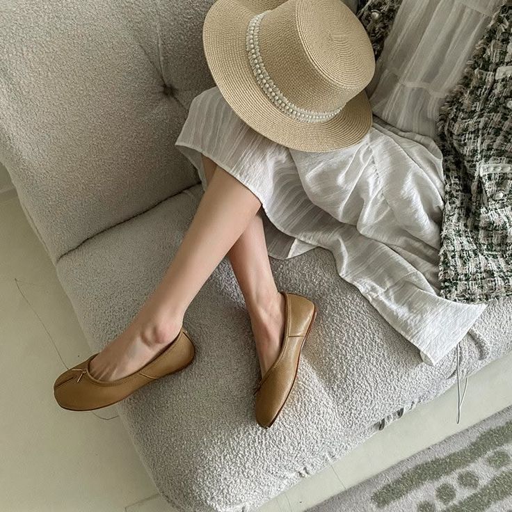 Person wearing a straw hat, white dress, and ballet flats sitting on a couch