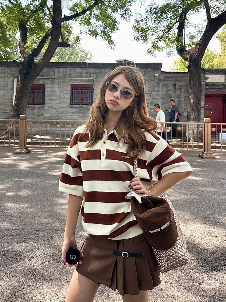 Woman in a striped polo shirt and pleated skirt posing outdoors