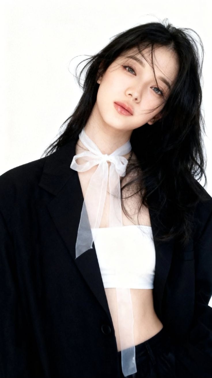 Woman with black hair wearing a white tube top and black blazer with a ribbon