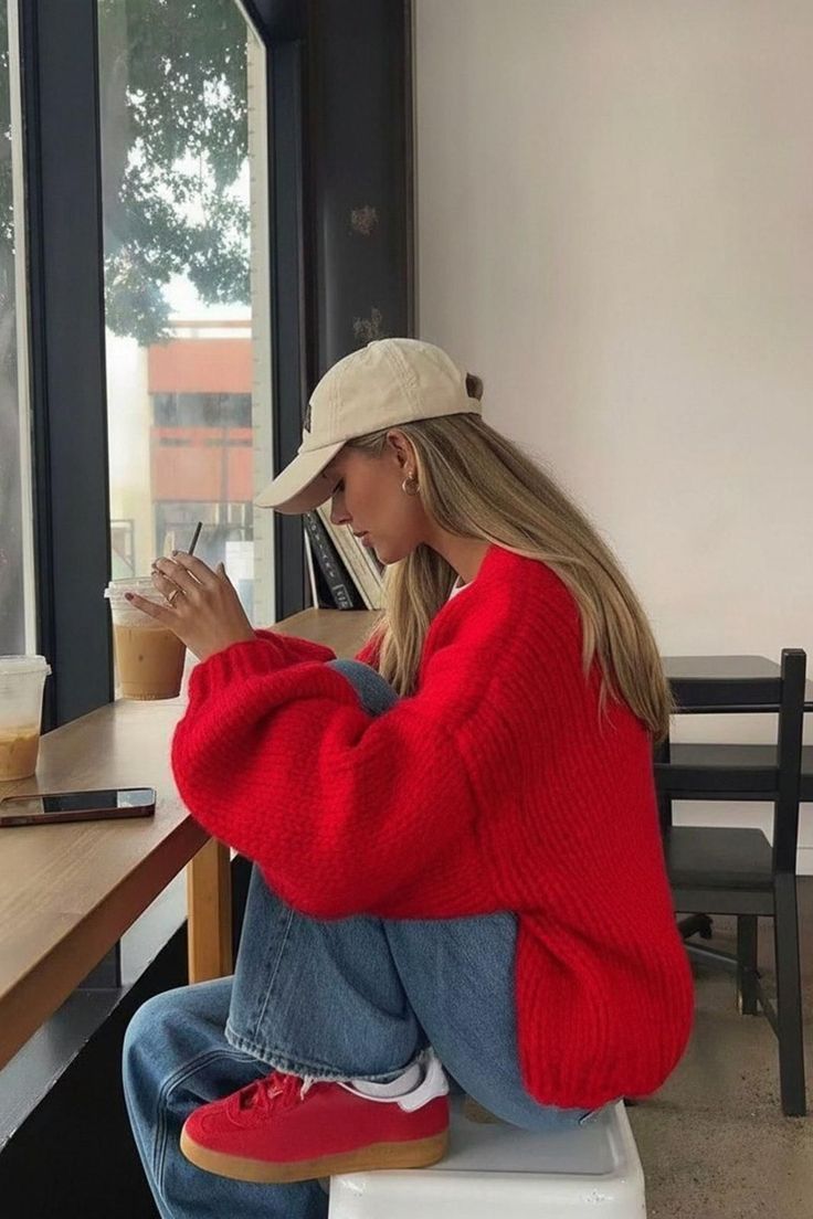 Woman in a red sweater and jeans drinking iced coffee at a cafe