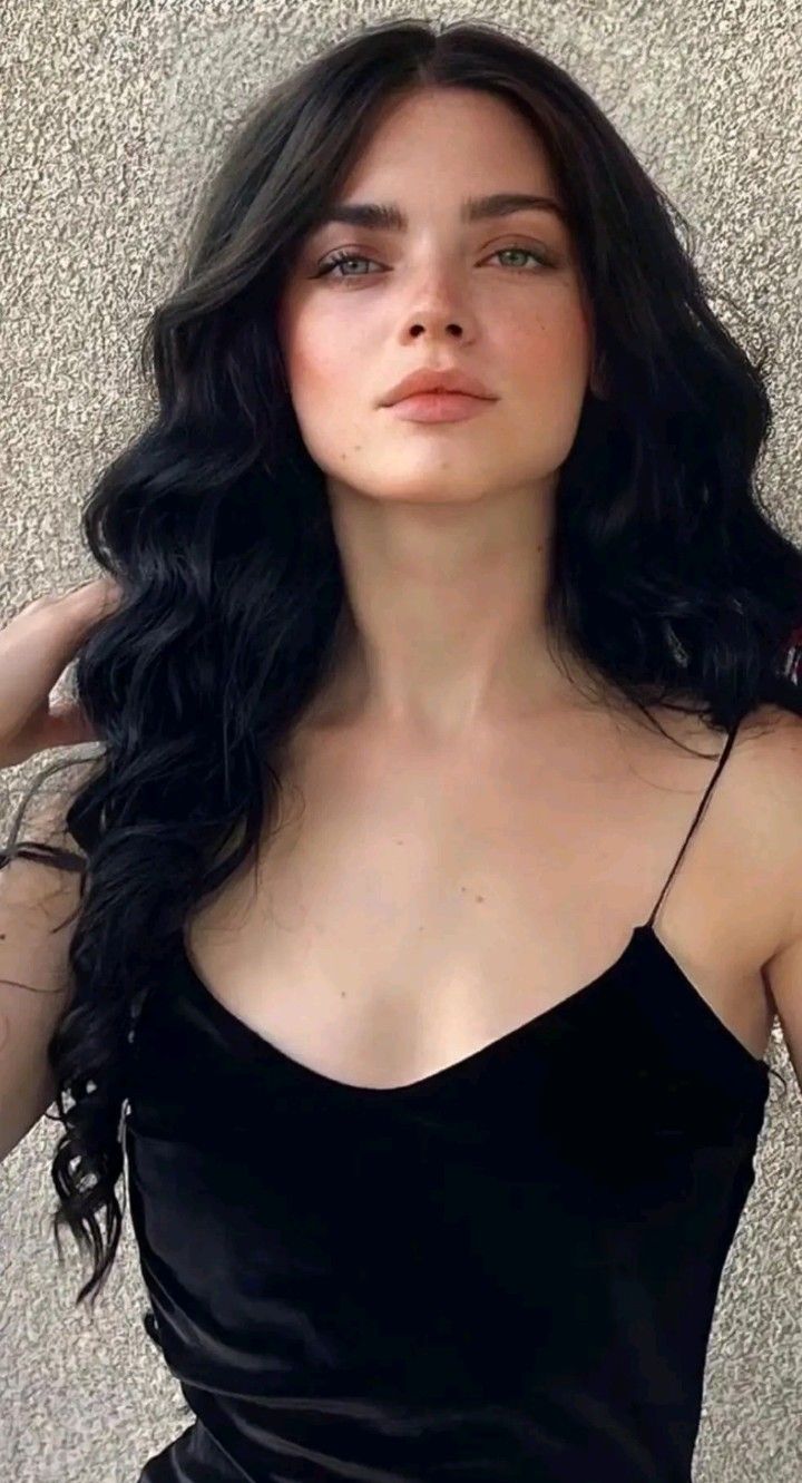 Woman with long black hair and green eyes wearing a black spaghetti strap top
