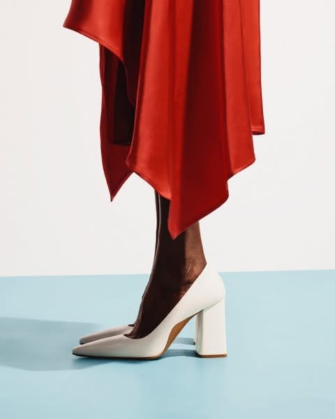 Person in a red dress and white heels against a blue and white background