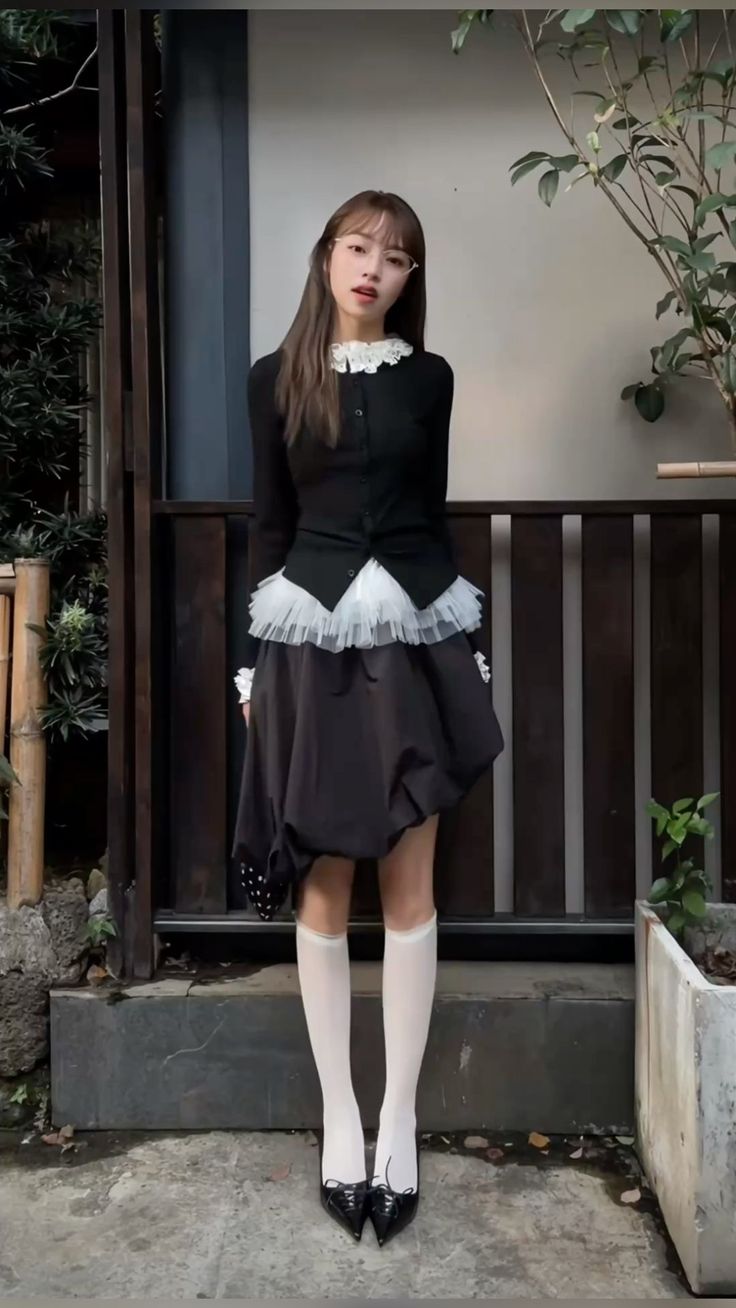 Woman in a black cardigan and bubble skirt with white knee socks and heels